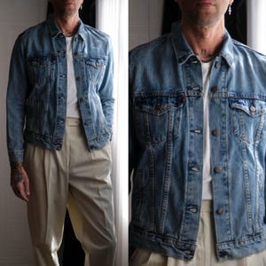 May include: A light blue denim jacket with a white t-shirt underneath. The person is wearing beige pants.