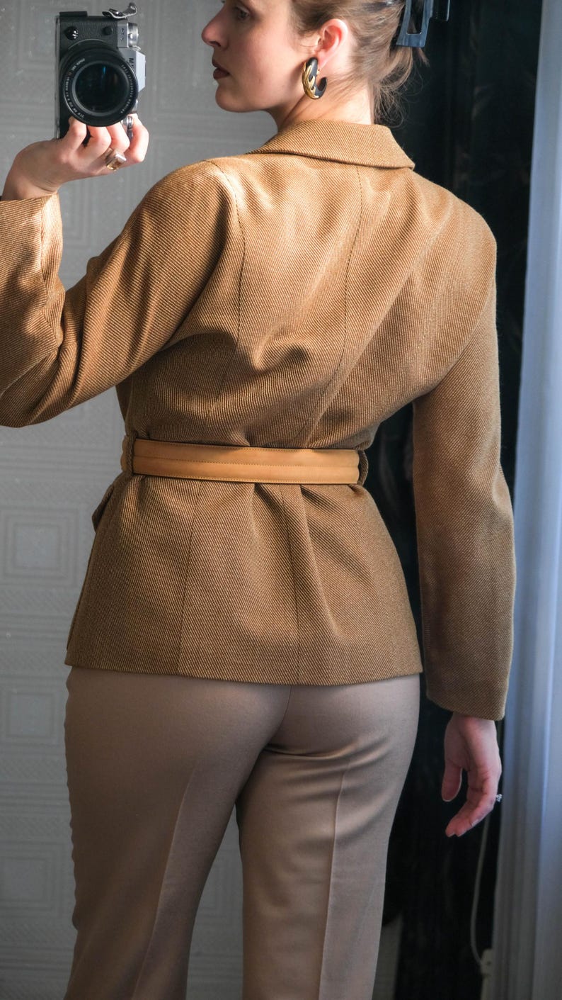 May include: A tan blazer with a matching belt cinches the waist, paired with tan trousers. The blazer has a tailored fit with subtle seam details. The outfit is a monochromatic ensemble, suitable for a professional or smart casual look.