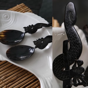 May include: Two dark, polished horn spoons featuring intricate, carved dragon-like motifs on the handles. The spoons have smooth, oval bowls with natural color variations, and the handles display detailed scale patterns and stylized head designs.