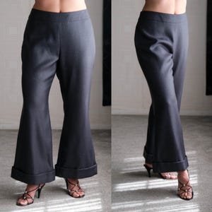 May include: Charcoal gray flared pants with a wide hem. The pants are shown from two angles, highlighting the tailored fit and the flared leg design. The pants are paired with black strappy heels.