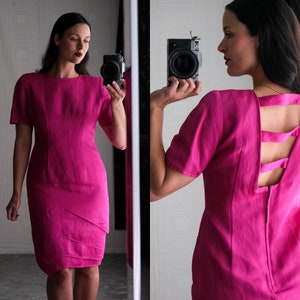 May include: A pink dress with a unique open back design featuring straps. The dress has a fitted bodice and a slightly flared skirt.