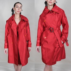 May include: A vibrant red trench coat with a double-breasted design, featuring a wide collar, belt, and button details. The coat has long sleeves with cuff straps and a knee-length hemline, offering a classic and stylish look.