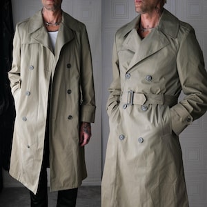 Op de afbeelding: Een beige trenchcoat met een dubbele rij knopen, met een reverskraag, knoopsluitingen en een riem in de taille. De jas heeft zakken en epauletten op de schouders. Een klassiek bovenkledingstuk.