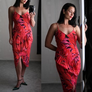 May include: A red, knee-length dress with a tropical leaf pattern in shades of red, pink, and black. The dress features a V-neck, spaghetti straps, and a front slit. The dress is made of a lightweight fabric.
