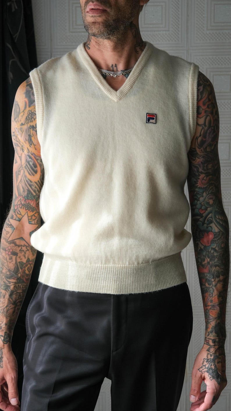 Peut inclure: Gilet sans manches cr&egrave;me &agrave; col en V avec un ourlet c&ocirc;tel&eacute; et un petit &eacute;cusson logo. Le gilet est sans manches et a une coupe d&eacute;contract&eacute;e. Le mod&egrave;le porte un pantalon noir.