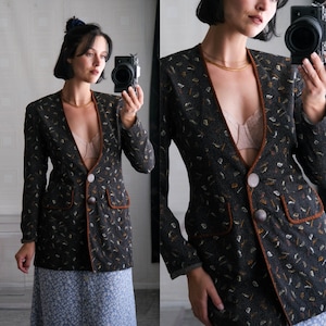 May include: A black blazer with brown trim and a small floral pattern. The blazer has a V-neck and a single button fastening.