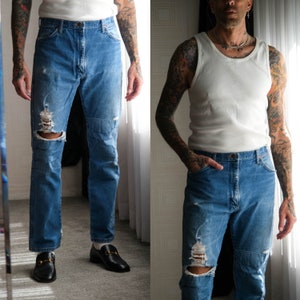 May include: Two photos of a person wearing a white tank top and blue jeans with distressed details and knee holes. The jeans have patches on the knees. The person is wearing black leather loafers with gold buckles.