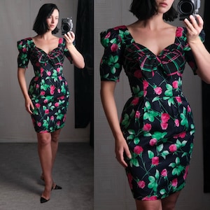 May include: A black dress with a floral print of pink and green roses. The dress has a sweetheart neckline and puffed sleeves. The dress is fitted and has a skirt that is slightly flared.