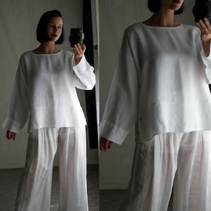 May include: A white linen top with long sleeves and a relaxed fit, paired with matching white linen pants. The outfit is loose and flowy, creating a comfortable and stylish look.