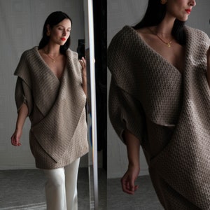May include: A brown knitted cardigan with a draped, asymmetrical design. The cardigan has a deep V-neck and long sleeves.