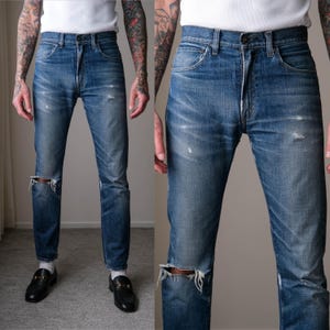 May include: Faded blue denim jeans with distressed details, including knee rips and subtle fading. The jeans have a classic five-pocket design and a straight-leg fit. The denim appears worn-in, with light distressing throughout.