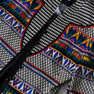 May include: A black and white patterned jacket with a colorful geometric design. The jacket has a button closure and a collar. The label reads "Anne Klein PAPPELL".