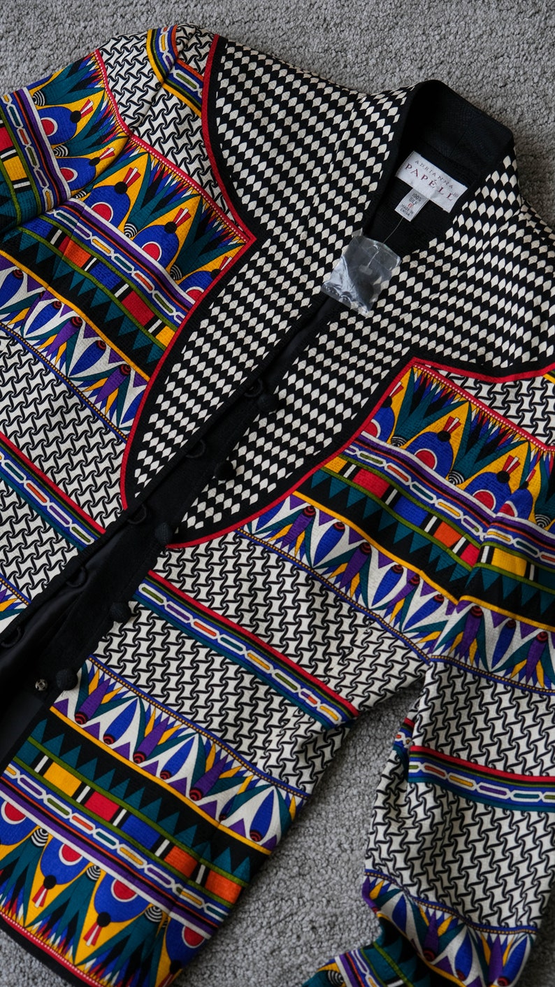 May include: A black and white patterned jacket with a colorful geometric design. The jacket has a button closure and a collar. The label reads "Anne Klein PAPPELL".