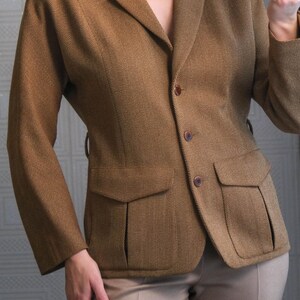May include: A brown blazer with a classic design, featuring a notched collar, two front pockets, and button closures. The blazer is paired with tan-colored trousers. The fabric has a subtle textured pattern.