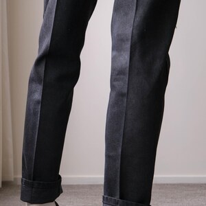 Peut inclure: Pantalon de costume noir avec revers et pli vertical discret. Le pantalon est associ&eacute; &agrave; des mocassins en cuir noir et des chaussettes blanches. L'ensemble est classique et &eacute;l&eacute;gant.