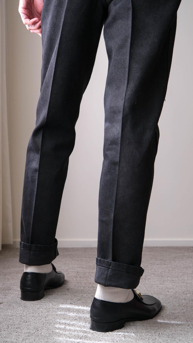 Peut inclure: Pantalon de costume noir avec revers et pli vertical discret. Le pantalon est associ&eacute; &agrave; des mocassins en cuir noir et des chaussettes blanches. L'ensemble est classique et &eacute;l&eacute;gant.
