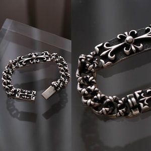 May include: A silver bracelet with a floral design. The bracelet features small, flower-shaped links forming a chain. The clasp and a central rectangular plate also have floral patterns.