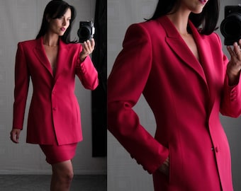 May include: A vibrant pink blazer and skirt suit. The blazer has a single button closure and a notched lapel. The skirt is a pencil skirt that falls just above the knee.