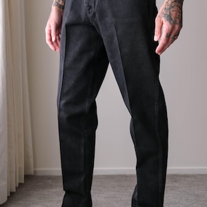 Peut inclure: Jean noir classique avec une coupe droite. Le jean a une fermeture boutonn&eacute;e et des poches. Le mod&egrave;le porte des mocassins en cuir noir avec des d&eacute;tails dor&eacute;s. La tenue est simple et &eacute;l&eacute;gante.
