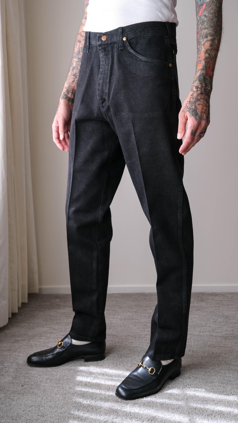 Peut inclure: Jean noir classique avec une coupe droite. Le jean a une fermeture boutonn&eacute;e et des poches. Le mod&egrave;le porte des mocassins en cuir noir avec des d&eacute;tails dor&eacute;s. La tenue est simple et &eacute;l&eacute;gante.