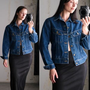 Puede incluir: Chaqueta vaquera clásica en azul medio, con cuello, cierre de botones y dos bolsillos en el pecho. La chaqueta tiene botones dorados y se combina con una falda negra. Las mangas están dobladas en las muñecas.