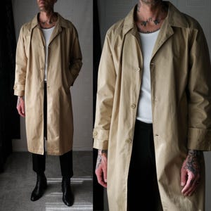 May include: A long beige trench coat with a button closure and a collar. The coat has a relaxed fit and is made of a lightweight fabric.