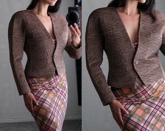 May include: A brown textured blazer with a v-neck and a single button closure. The blazer is worn over a plaid skirt.