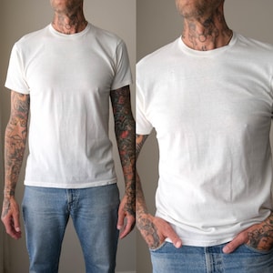 May include: A plain white short-sleeved t-shirt with a crew neckline, paired with light blue denim jeans. The t-shirt features a simple, solid-coloured design with a standard fit, constructed from a lightweight fabric, worn with classic blue jeans.