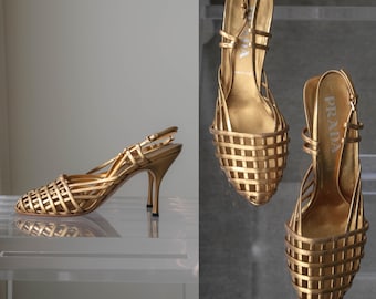 Puede incluir: Un par de zapatos de tacón destalonados en oro metalizado con un empeine tejido tipo jaula de tiras finas, punta afilada y tacón fino. La plantilla interior lleva estampado el nombre de la marca Prada en blanco.