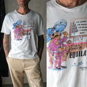 May include: White t-shirt featuring a colorful cartoon of a mustached man in a sombrero at a bar, with the text "THE 4 STAGES OF TEQUILA" and "TIJUANA Mexico". The shirt also has the text "I'M QUIET, I'M HAPPY, I'M HANGRY, I DON'T SHIT!"