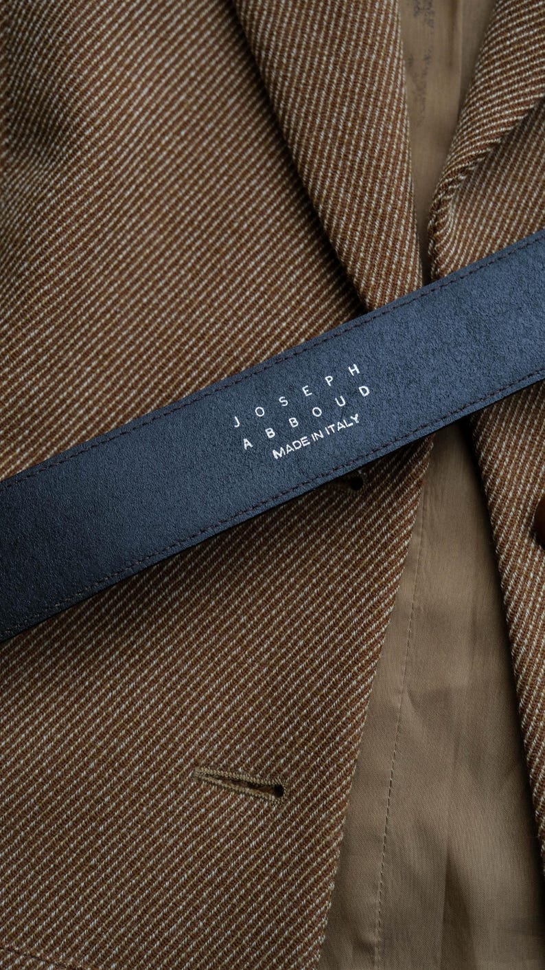 May include: A close-up of a black leather belt with the text "JOSEPH ABBOUD MADE IN ITALY" in white. The belt is positioned over a brown and tan tweed blazer.