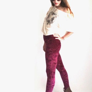 Puede incluir: Una mujer con una camisa blanca con estampado gráfico y leggings de terciopelo burdeos. Lleva gafas redondas y botas marrones.