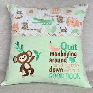 May include: A decorative cushion with a light green base and a top section featuring a jungle animal print. The cushion has an embroidered monkey design with the text "Quit monkeying around and settle down with a GOOD BOOK."