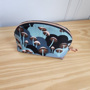 May include: A blue and black zippered pouch with a mushroom print. The pouch has a rose gold zipper and a rose gold pull tab.