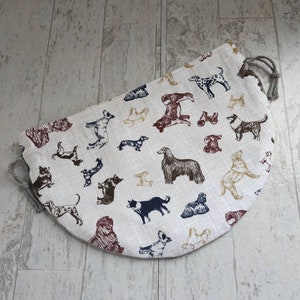 May include: A beige fabric storage bag with a drawstring closure. The bag is decorated with a repeating pattern of black, brown, and white dogs.