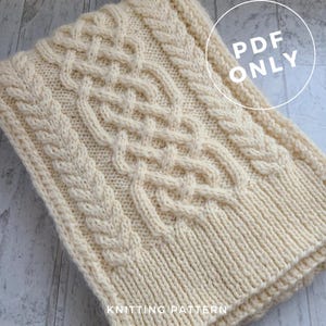 Puede incluir: Una bufanda de punto de color crema con un patrón de trenza. La bufanda está hecha con un hilo grueso y tiene una superficie texturizada. El texto "PDF ONLY" está impreso en un círculo blanco en la esquina superior derecha de la imagen. El texto "KNITTING PATTERN" está impreso en la esquina inferior derecha de la imagen.
