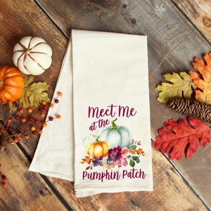 May include: White tea towel with a watercolor design of pumpkins, flowers, and leaves. The text "Meet me at the Pumpkin Patch" is printed in purple.