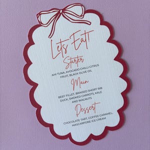 Op de afbeelding: Een menukaart met een geschulpte rode rand en een strikdesign bovenaan. Het menu toont de woorden "Let's Eat!" in rood schrift, gevolgd door de voorgerecht-, hoofdgerecht- en dessertopties.