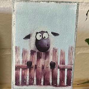 May include: A rectangular wooden sign depicts a sheep looking over a wooden fence. The sheep has a black face and large eyes. The sign has the text "mentally somewhere else" at the bottom.
