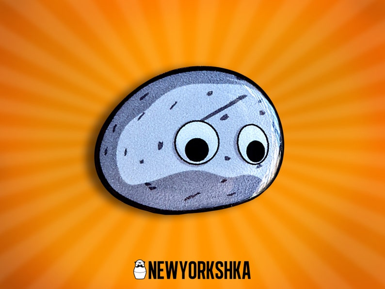 May include: A cartoon-style rock with googly eyes, set against an orange burst background. The rock is gray with black speckles and a black outline. The logo "NEWYORKSHKA" is at the bottom.
