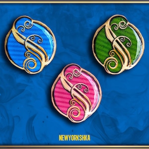 May include: Three decorative oval-shaped pins with a gold-colored filigree design. Each pin features a different color: blue, green, and pink. The background is a deep blue with gold accents. The text "NEWYORKSHKA" is visible at the bottom.