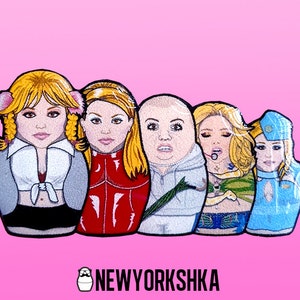 May include: A set of five nesting dolls featuring illustrations of a blonde woman in various outfits. The dolls are set against a pink background, with the text "NEWYORKSHKA" at the bottom.
