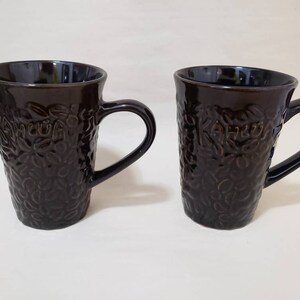 May include: Two brown ceramic coffee mugs with a textured design of coffee beans and the word "Kahula" on the side.