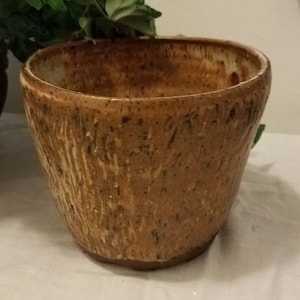 May include: A brown ceramic planter with a textured surface. The planter has a wide, round opening and a slightly flared lip.