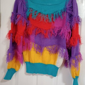 May include: A multi-colored sweater with a rainbow pattern and fringe trim. The sweater is made of a soft, knit fabric and has a relaxed fit.