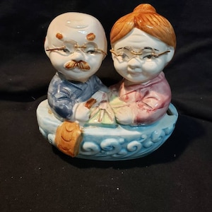 Ceramic piggy bank of an old cuddling couple in a boat with their eyeglasses.