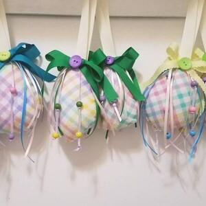May include: Four pastel plaid Easter eggs with colorful ribbons and beads hanging from white string.
