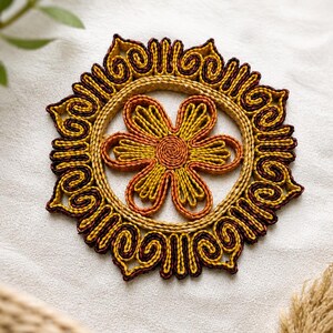 May include: A handcrafted coaster with a floral design. The coaster features a central flower with yellow and orange petals, surrounded by a decorative border in shades of brown and yellow. The coaster is made of woven natural fibers.