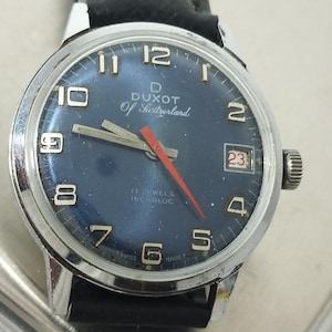 Könnte beinhalten: Eine Vintage-Duxot-Armbanduhr mit dunkelblauem Zifferblatt, silbernen Zeigern und einem roten Sekundenzeiger. Die Uhr hat ein silbernes Gehäuse, ein schwarzes Lederarmband und eine Datumsanzeige auf 3 Uhr. Das Zifferblatt zeigt den Text "Duxot Of Switzerland".