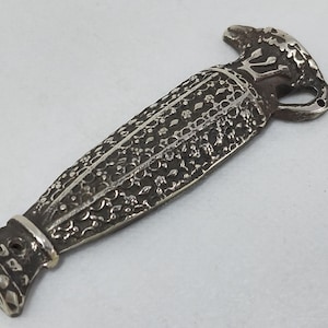 Może przedstawiać: Srebrny metalowy korek do butelki o ozdobnym wzorze. Korek ma szczegółowy kwiatowy wzór i uchwyt z małym otworem. Projekt przypomina starożytne artefakty.